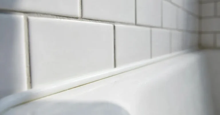 Freshly caulked white bathtub with a smooth silicone bead along the tile wall