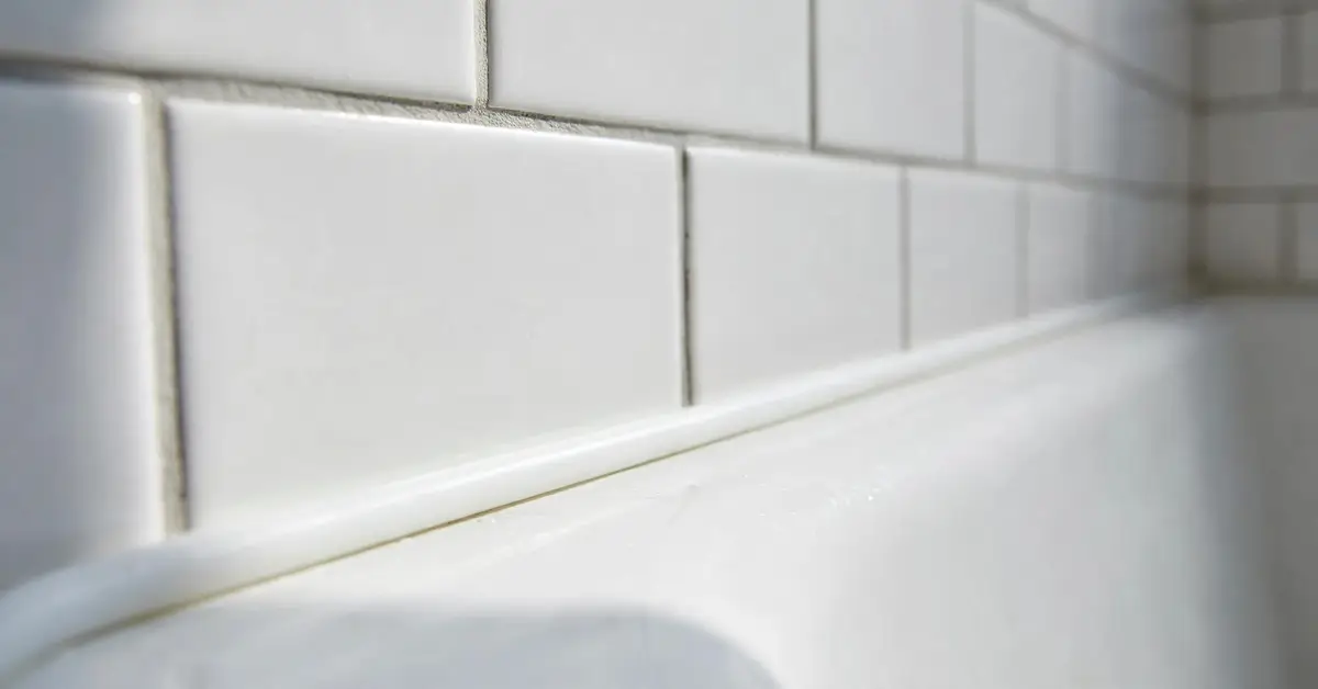 Freshly caulked white bathtub with a smooth silicone bead along the tile wall