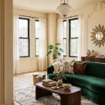 Art Deco apartment living room with a curved emerald velvet sofa, geometric rug, walnut furniture, and brass lighting.