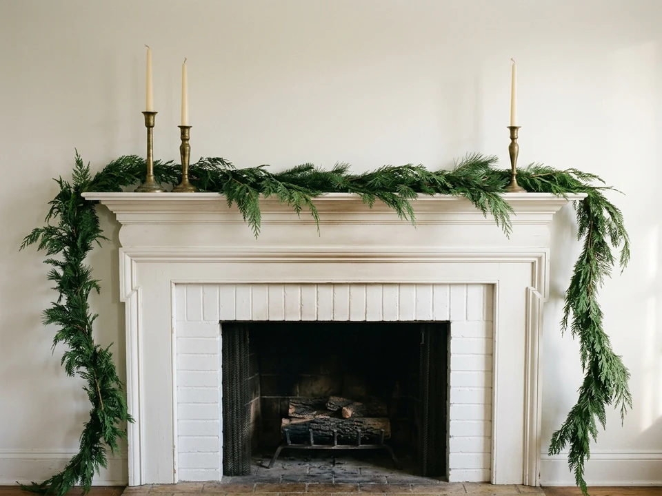 Fireplace mantel with loose evergreen garland and tall brass candlesticks