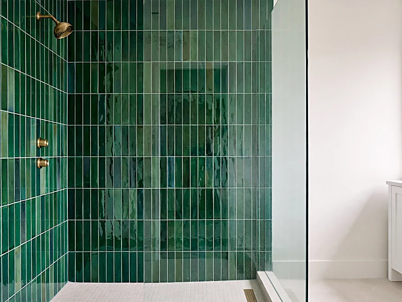 Walk-in shower with glossy emerald green wall tiles, clear glass enclosure, and brass shower fixtures.