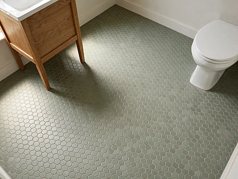 Sage green hexagon bathroom floor tiles beneath an oak vanity and white bathroom fixtures.