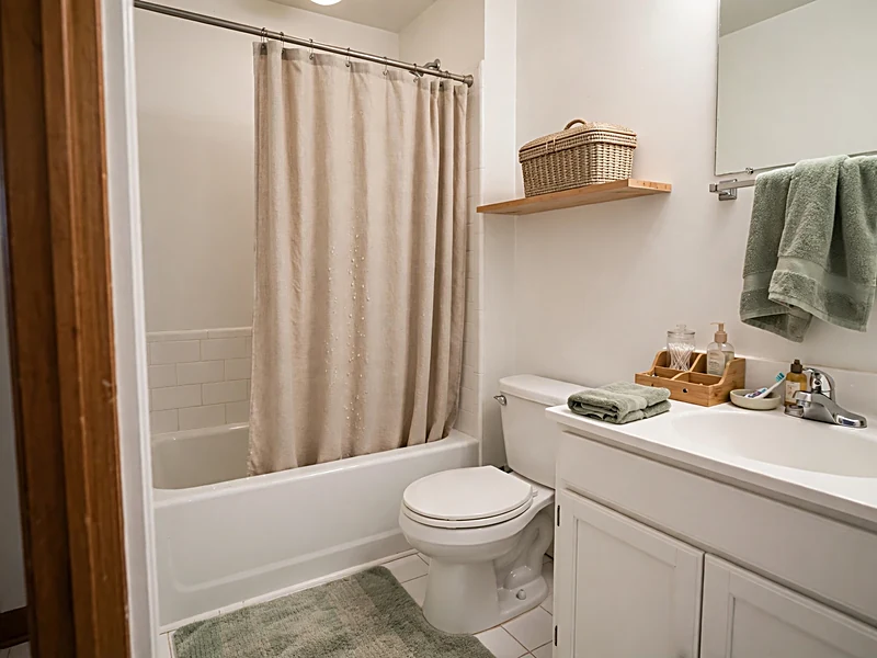 Small rental bathroom with a coordinated shower curtain, sage towels, bath mat, and organized sink storage.
