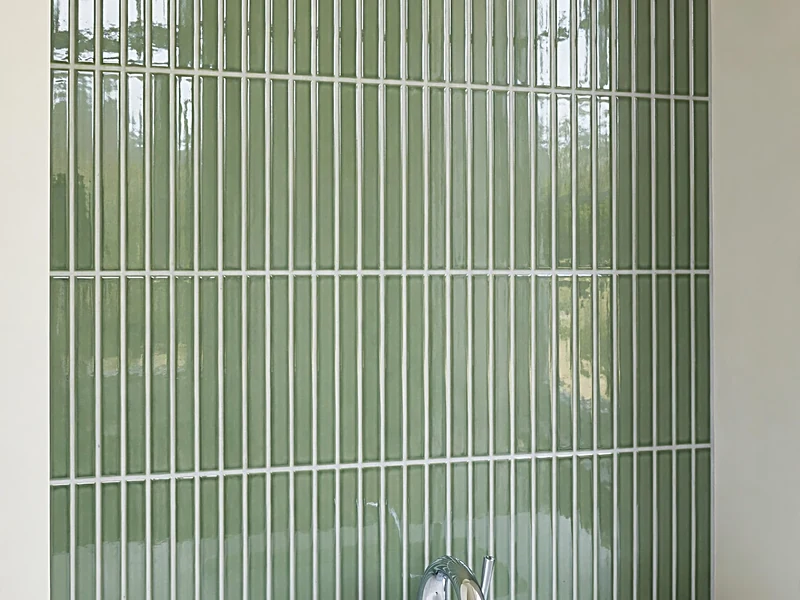 Shower wall with vertically stacked sage green subway tiles, matching grout, and chrome shower fixtures.